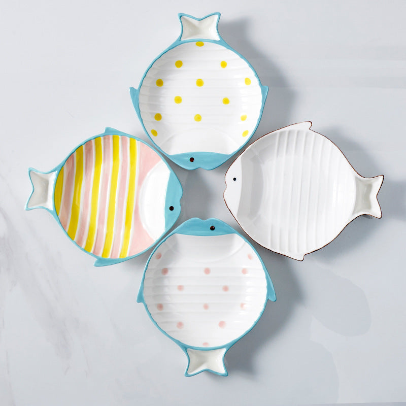 Top-down flat lay of fish-shaped ceramic cat bowls in four colors arranged in a square pattern