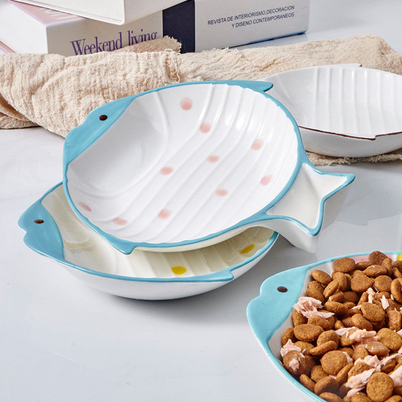 Stacked fish-shaped ceramic cat bowls in pink and yellow polka-dot designs with blue trim, displayed on a kitchen counter